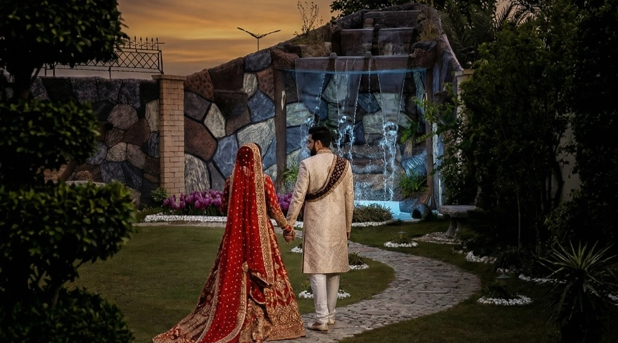 Bride and groom walking in garden with waterfall backdrop at AH Royal Resort, ideal for romantic photoshoots in Islamabad