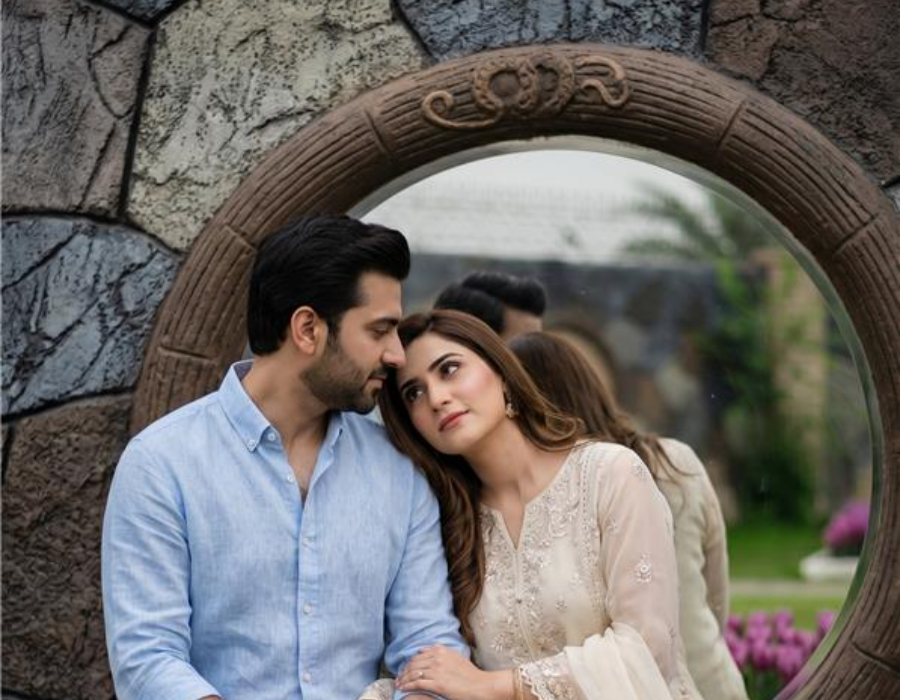 Romantic couple sitting by a garden mirror wall with flowers during an intimate anniversary photoshoot at a farmhouse in Islamabad